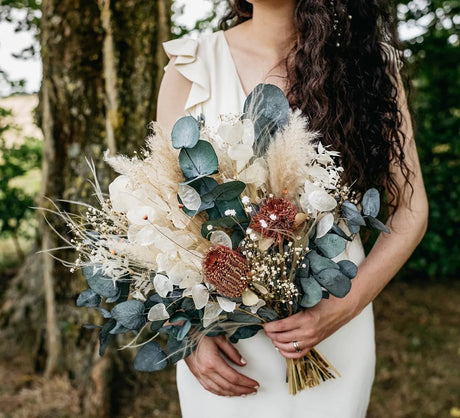 Wedding bouquet containing eucalyptus held by a bride dressed in a white dress.