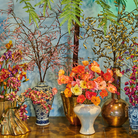 A table-top display of boldly coloured faux flowers arranged in a variety of different vases.