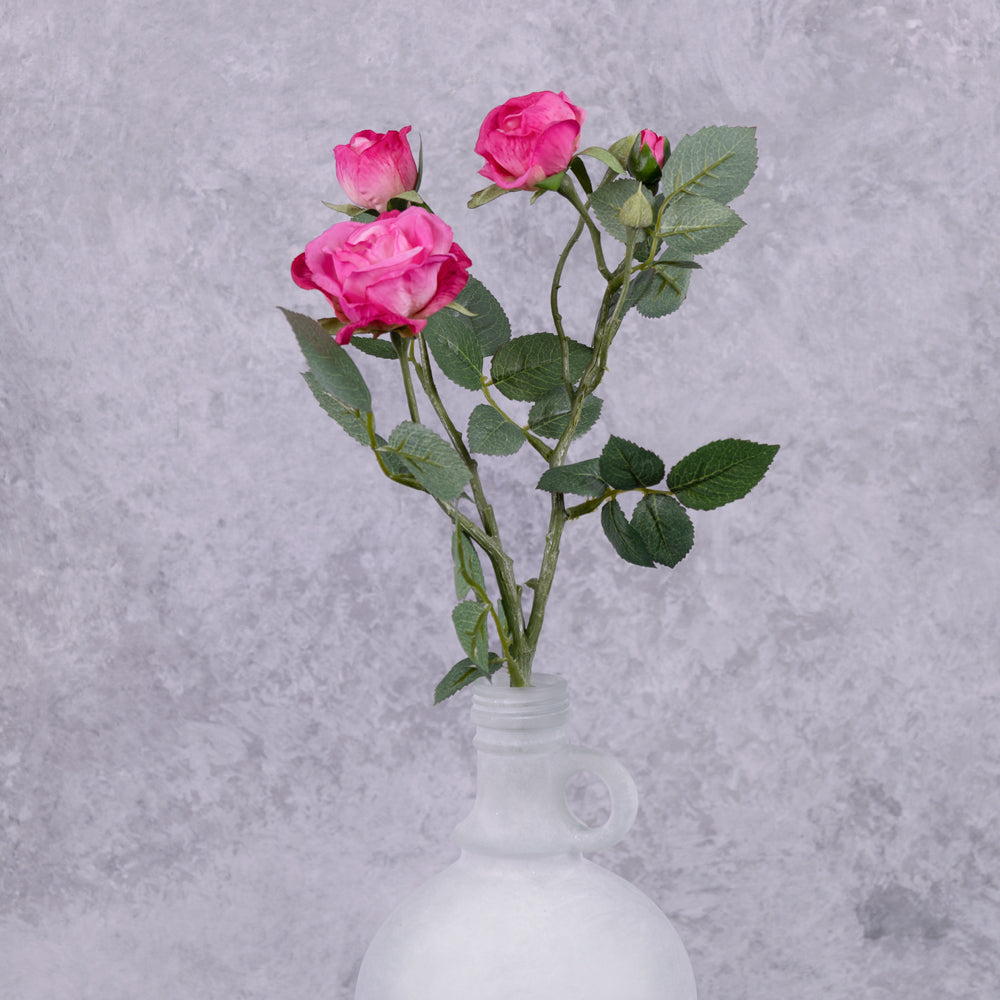 A faux dark pink rose spray shown in a frosted white glass vase