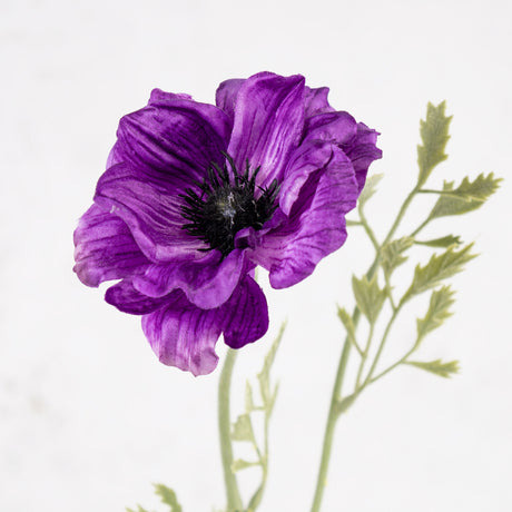 A faux anemone flower and stem with leaf detail, in purple.
