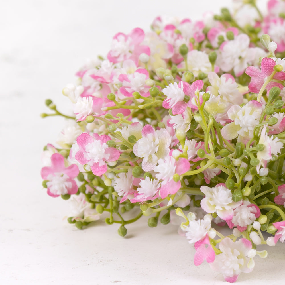 A close up of an artificial gypsophila wreath with pink and white flowers, on a green plastic frame.