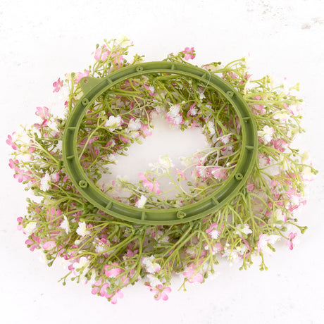 An artificial gypsophila wreath with pink and white flowers, on a green plastic frame.