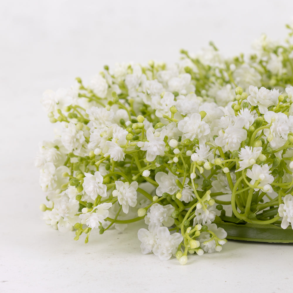 An artificial gypsophila wreath with white flowers, on a green plastic frame.