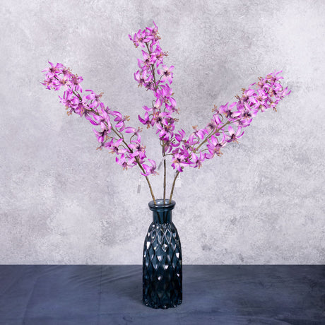 Three faux lily stems in a deep pinkish purple colour, shown in a blue glass vase