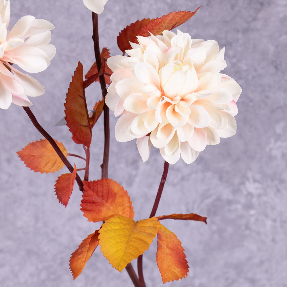 A close up of a faux dahlia flower in pale pink with rusty orange leaves.