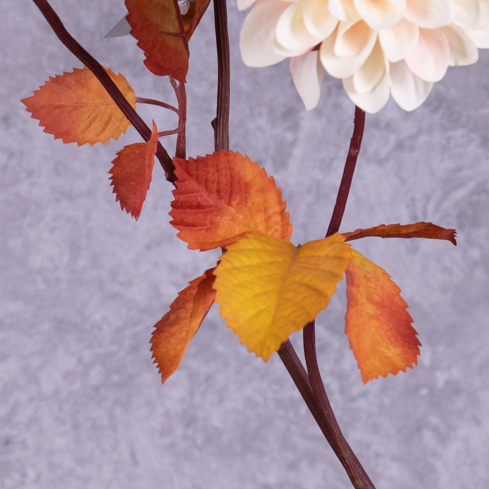 A close up of a faux dahlia flower stem with rusty orange leaves.