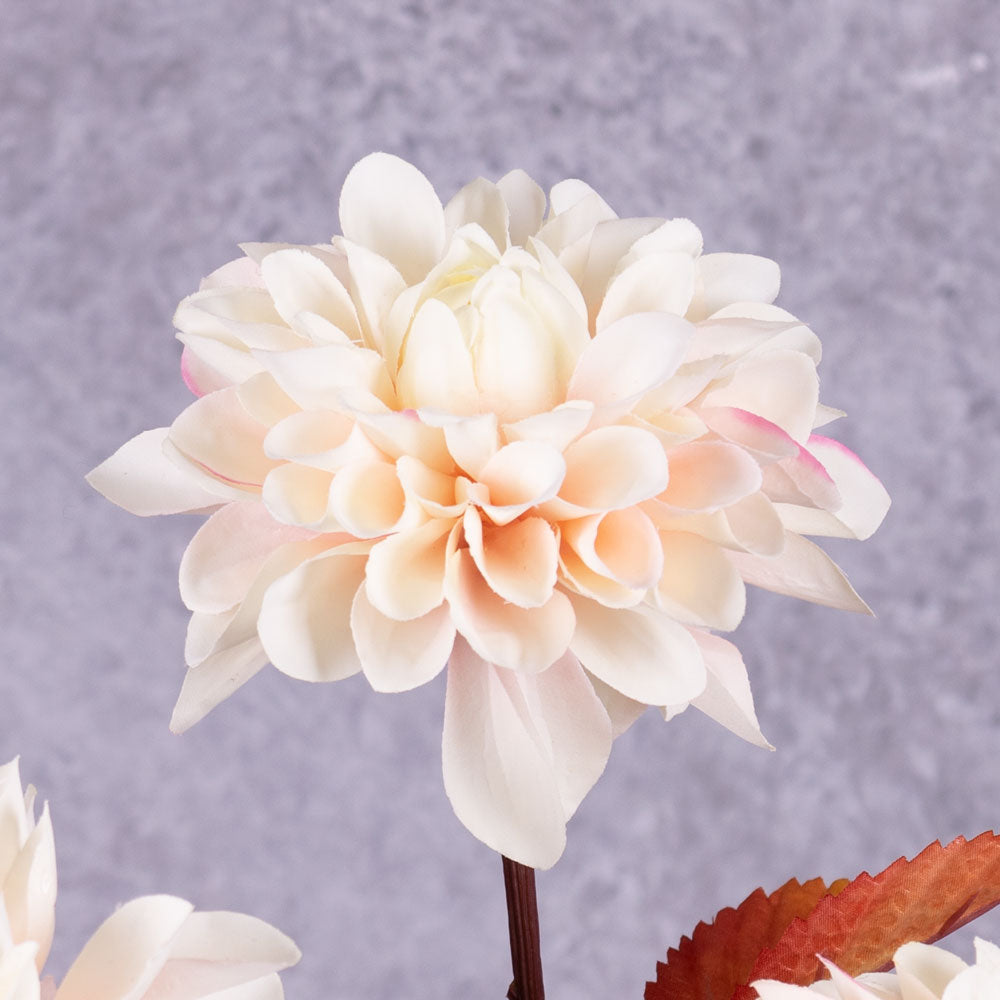 A close up of a faux dahlia flower in pale pink with rusty orange leaves.