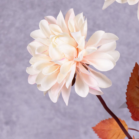 A close up of a faux dahlia flower in pale pink with rusty orange leaves.