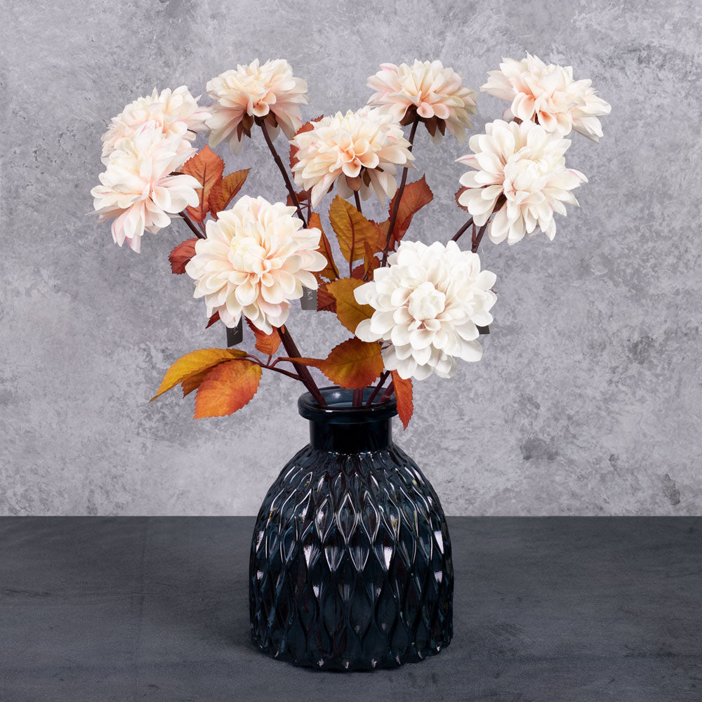 A group of three faux dahlia sprays with large, pale pink flowers and rusty orange leaves, displayed in a blue glass vase.