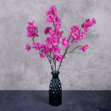 Three faux Bougainvillea stems with bright pink flowers over several branchlets, shown in a blue glass vase