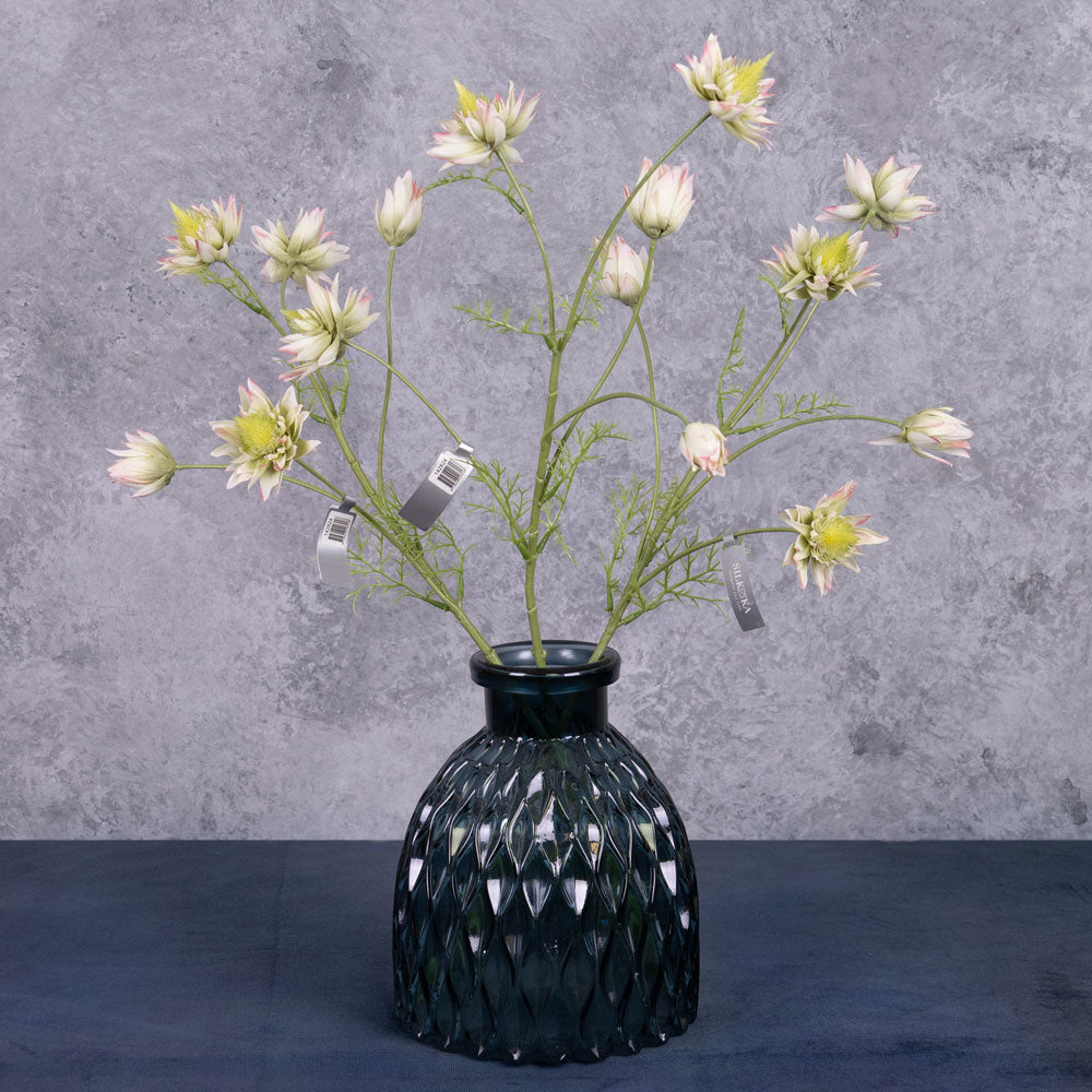 Three faux protea stems in a green/pink colour, displayed in a blue glass vase