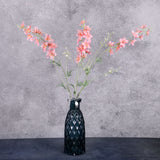Three tall faux delphinium stems with pink flowers and buds on stems, in a blue glass vase