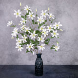 A group of three large faux clematis stems in white, shown in a blue glass vase