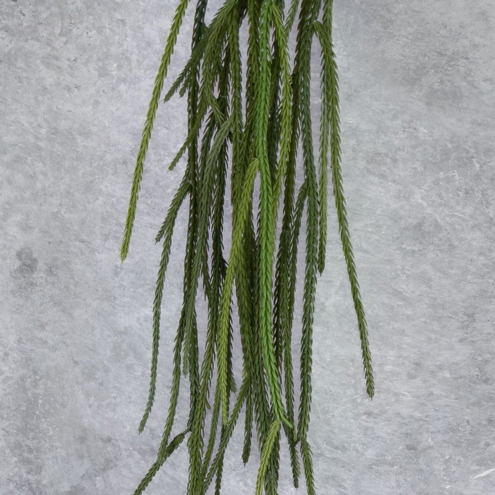 A close up of the mid-section of a single, faux, green, hanging grass plant.