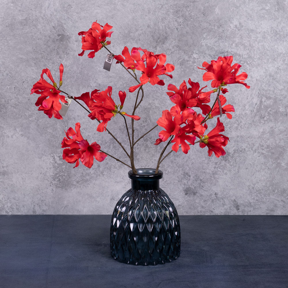 Thrree faux mandevilla sprays with several red flowers, shown in a blue glass vase