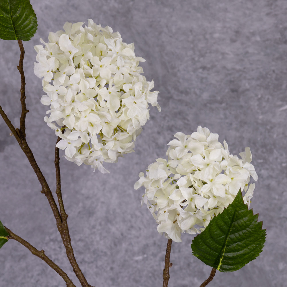 A close up of a faux, cream hydrangea flower that looks like a pom pom, showing leaf detail