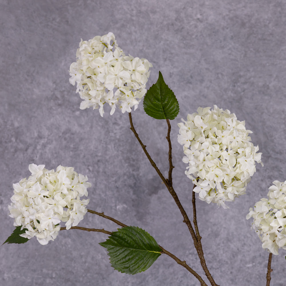 A close up of a faux, cream hydrangea flower that looks like a pom pom, showing leaf detail