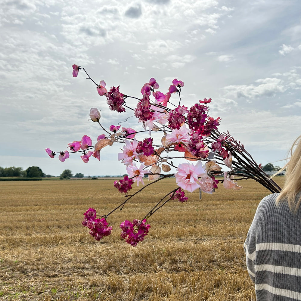 A stunning group of different artificial flowers in various shades of pink, set against a background of a cloudy sky, and stubble field.