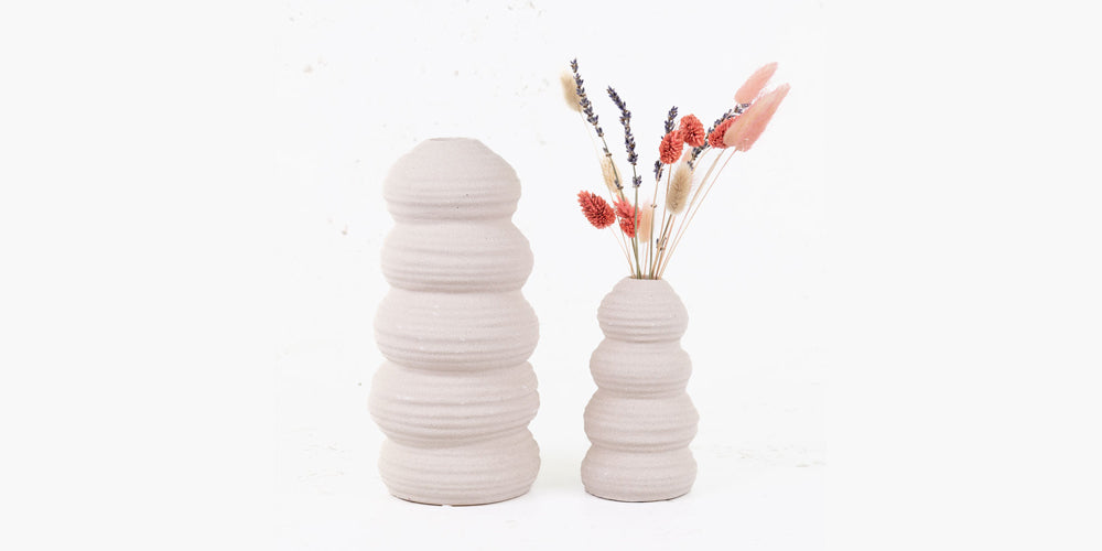 A pair of cream coloured stone vases in different heights. the smaller containing some dried flowers
