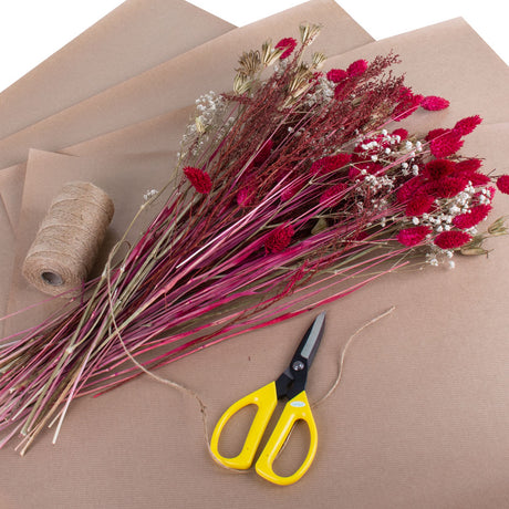 Beautiful red and natural dried flowers laid against brown paper alongside scissors and brown twine.