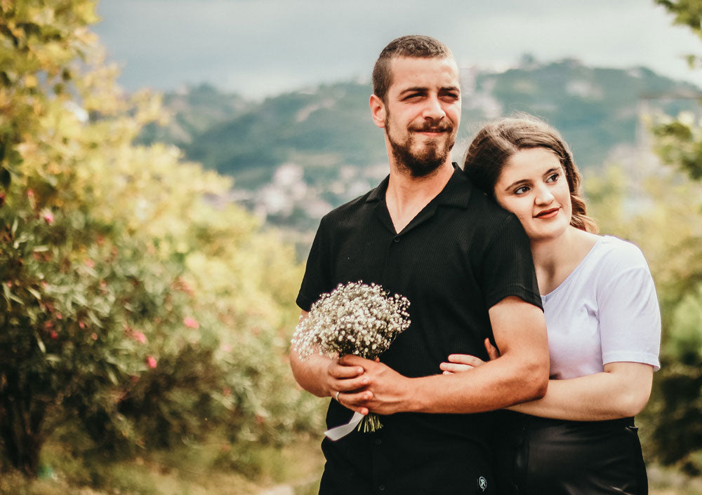 Photo of a couple standing in the countryside, with the man holding a gypsophila bouquet, by Yusuf Kahriman
