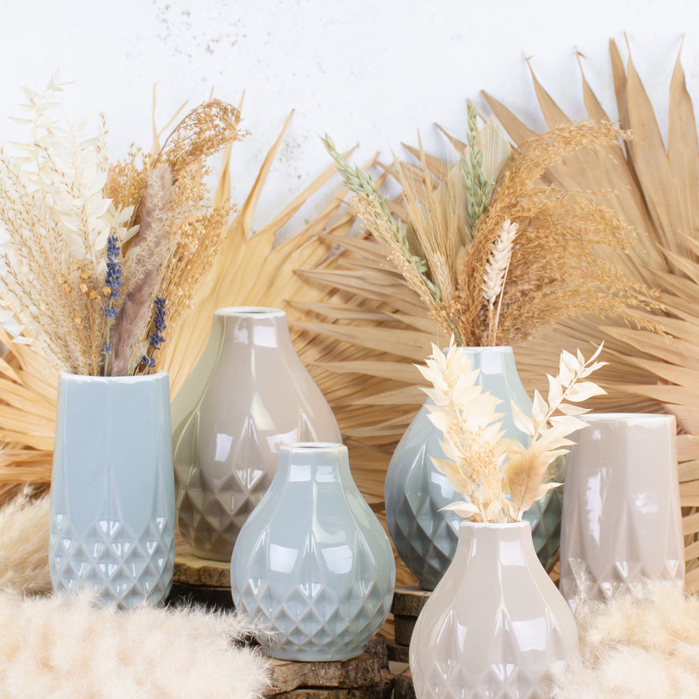 A group of different sized and coloured vases of a similar style, showing dried flowers.