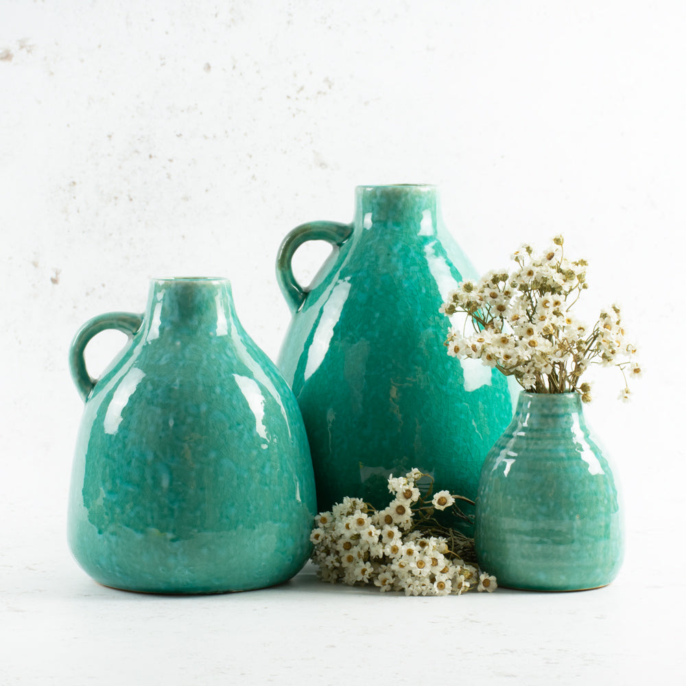 Mixed size turquoise bottle vases displaying some dried flowers