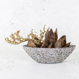 A boat-shaped stone bowl with flower detailing to the surface, shown holding dried sorocca flowers, displayed alongside gold canella.