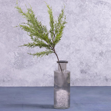 A faux juniper stem displayed in a glass vase