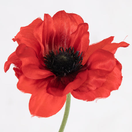 A close up of a faux anemone flower in bright red.