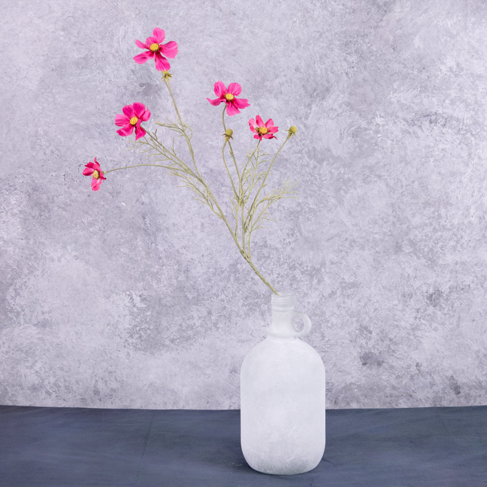 A pink cosmos flower spray displayed in a white frosted glass demi-john