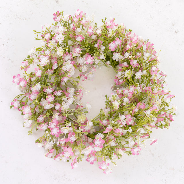 An artificial gypsophila wreath with pink and white flowers, on a green plastic frame.