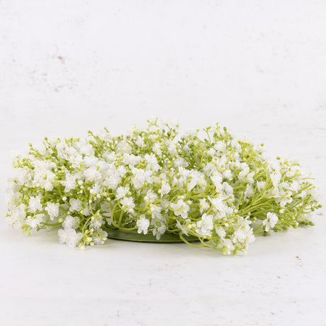 An artificial gypsophila wreath with white flowers, on a green plastic frame.