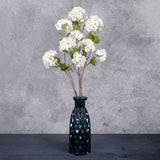 Three faux viburnum, or snowball flowers, in white, displayed in a blue glass vase