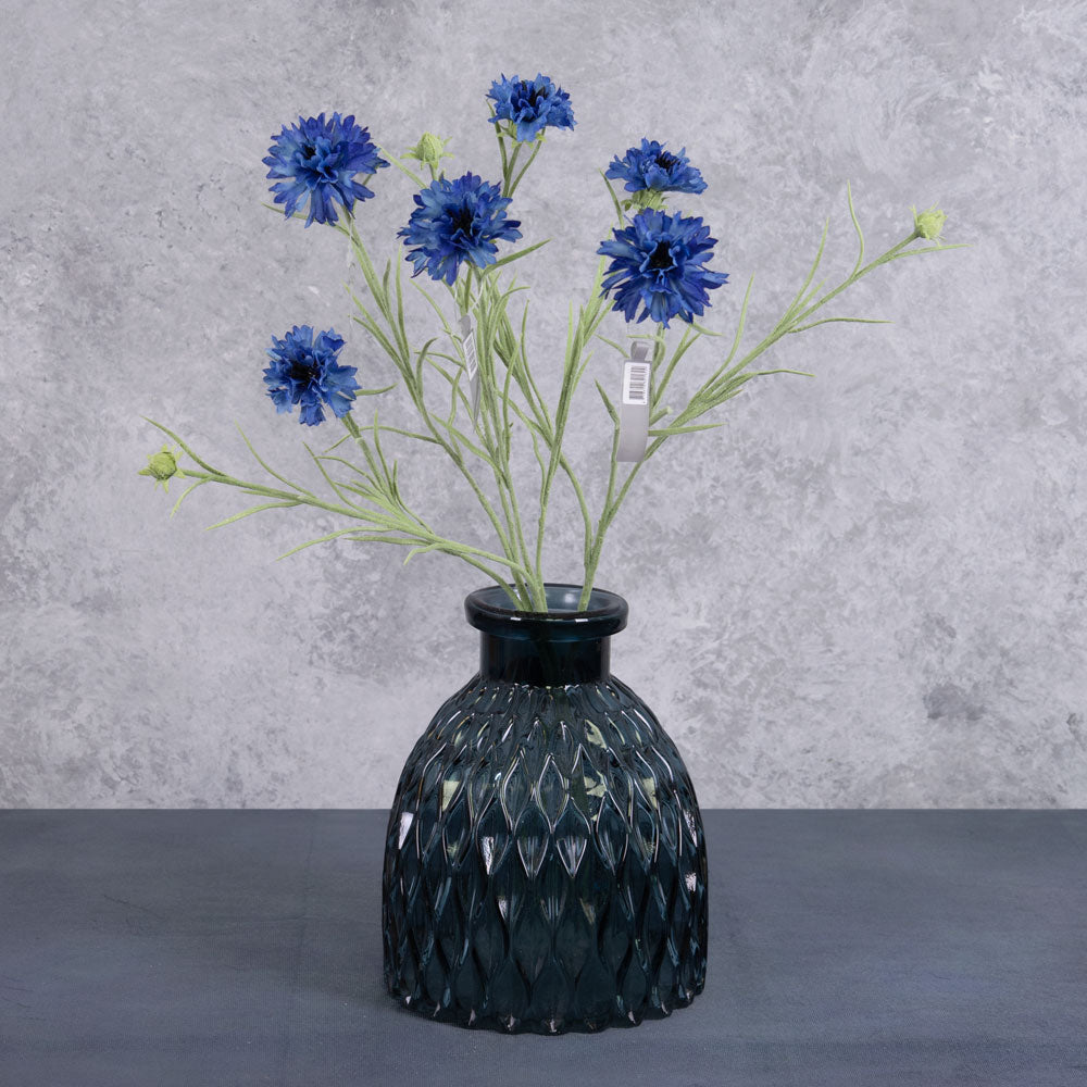 A group of three deep blue cornflower stems, displayed in a blue glass vase.