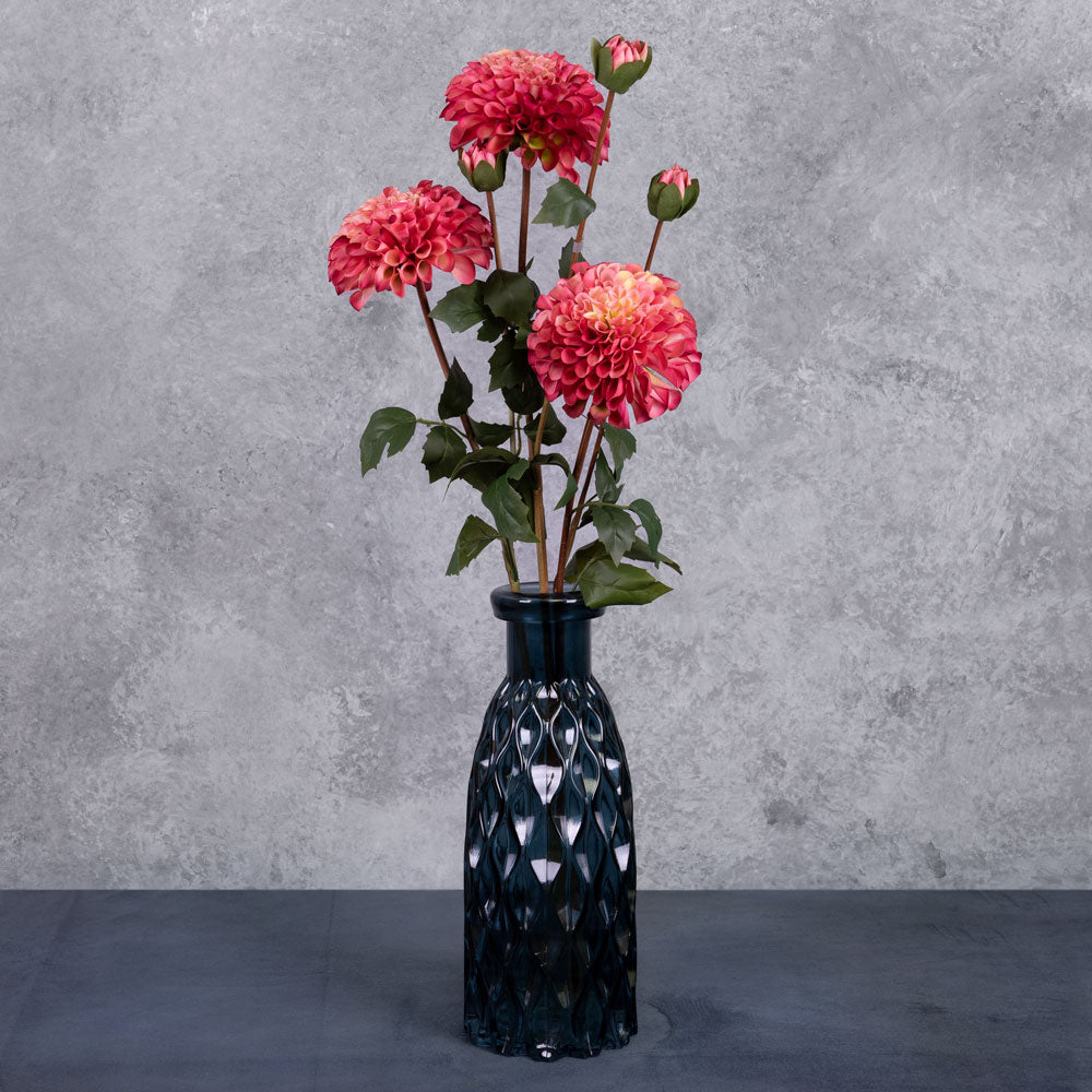 Three faux dahlia sprays in a deep pink colour, displayed in a blue glass vase