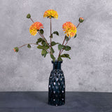 Three faux dahlia sprays in a rich red-orange colour, with both flowers and buds, all in a blue, glass vase