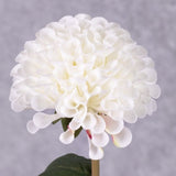 A close up of a faux, white dahlia bud and pom pom flower with leaves