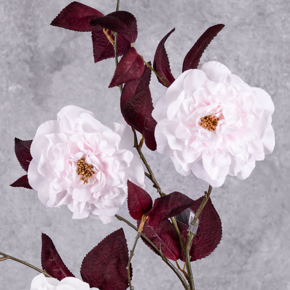 A close up of a faux camelia spray, in white with red leaves