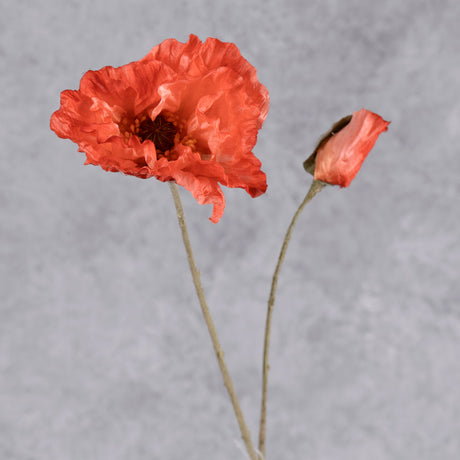 A close up of a faux poppy flower, and a bud, in a delicate reddish orange