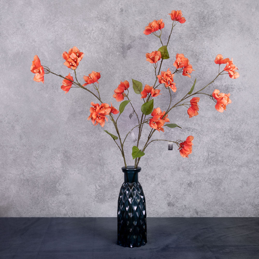 Three faux bougainvillea stems in an acidic red-orange colour, shown in a blue glass vase