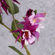 A close up of a pair of faux aquilegia flowers in a warm purple hue, and pinkish centre, and leaves over several branchlets