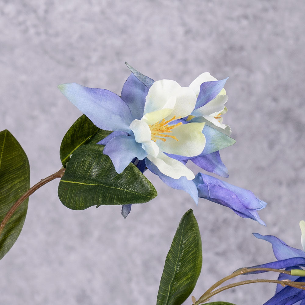 A close up of a faux aquilegia flower in a blue hue, and white centre