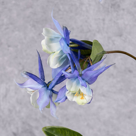 A close up of three faux aquilegia flowers in a blue hue, and white centre