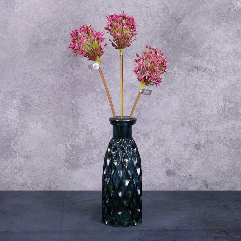 A group of three faux allium stems with deep pink coloured flower plumes, displayed in a blue glass vase