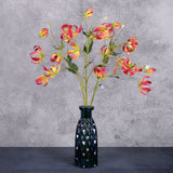A group of three faux gloriosa sprays with pink-yellow flowers, displayed in a blue glass vase