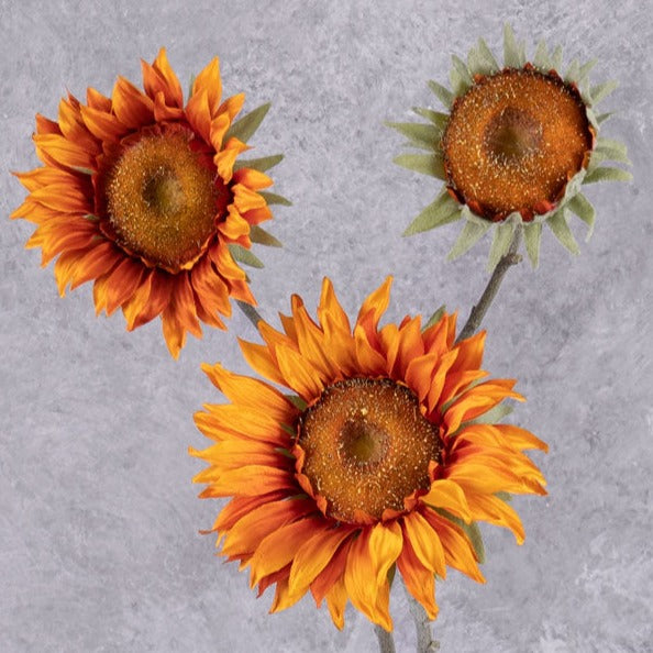 A faux sunflower spray in a rich orange colour., showing three flowers