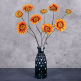 A group of three faux sunflower sprays in a rich orange colour, displayed in a blue glass vase