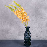 Three faux eremurus stems with peachy-yellow flowers, shown in a blue glass vase