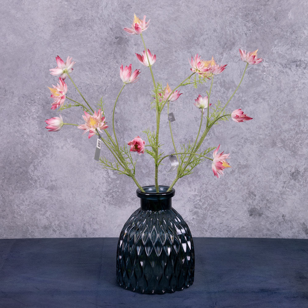 A group of three faux Protea stems with lots of flowers in a pink/white colour, displayed in a blue glass vase